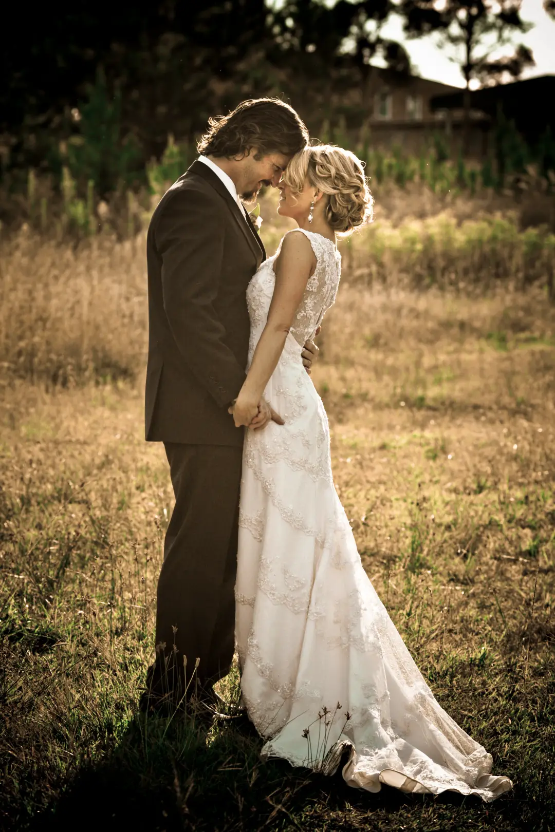 Bride and groom in a paddock at sunset, the bride in a lace gown with her hair in a soft updo