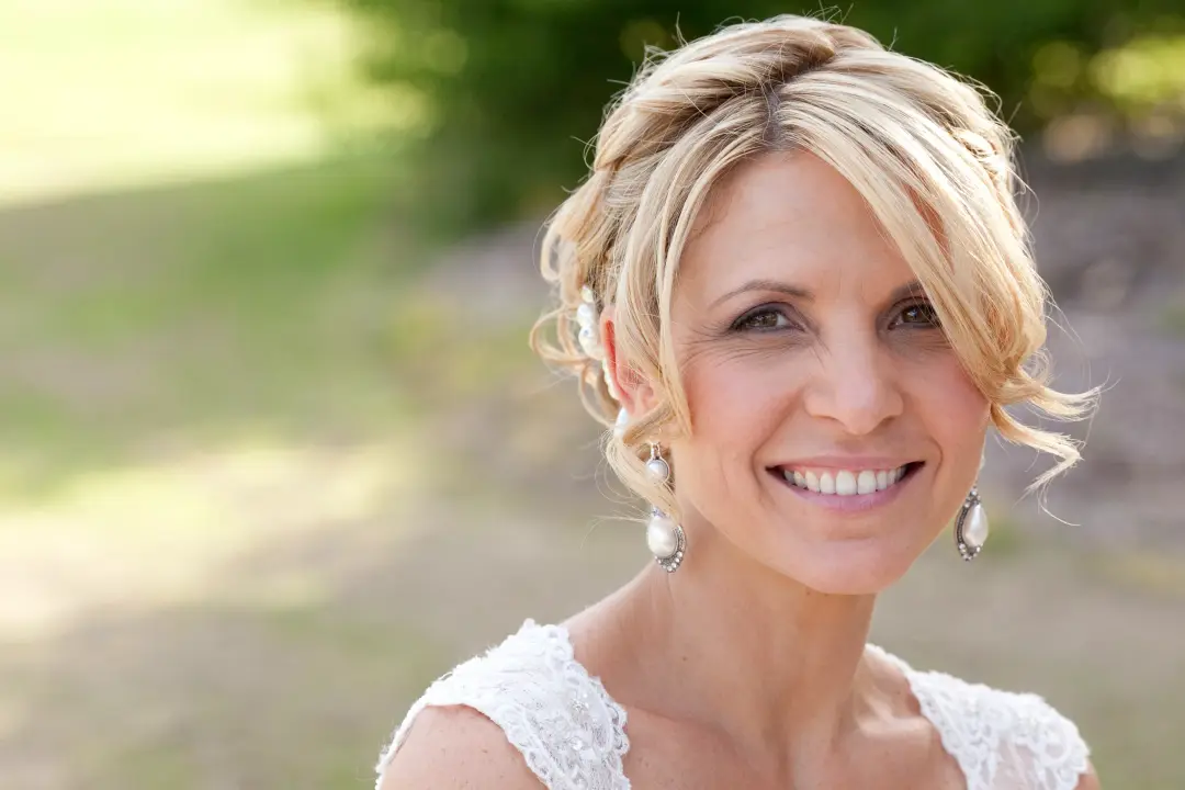 Bride in a soft twisted updo with tendrils at the temples, wearing natural makeup and pearl earrings, by Amanda Frost of Bellus