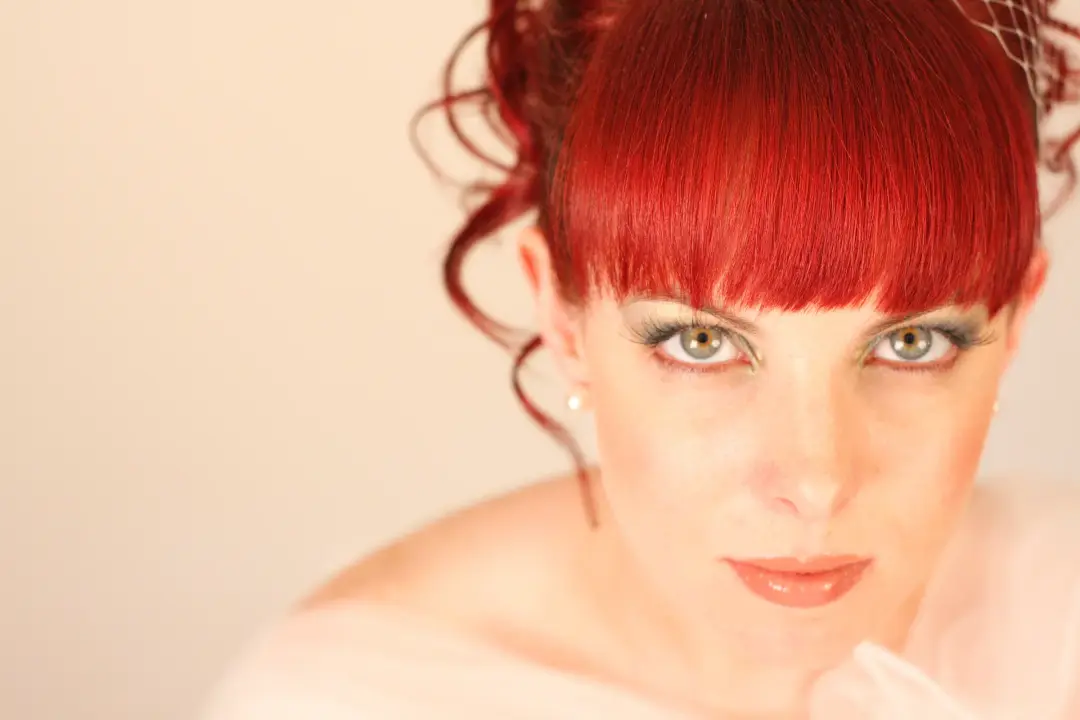 Bold sophisticated makeup with a green tinted eye and a strong lip, worn with a red fringe
