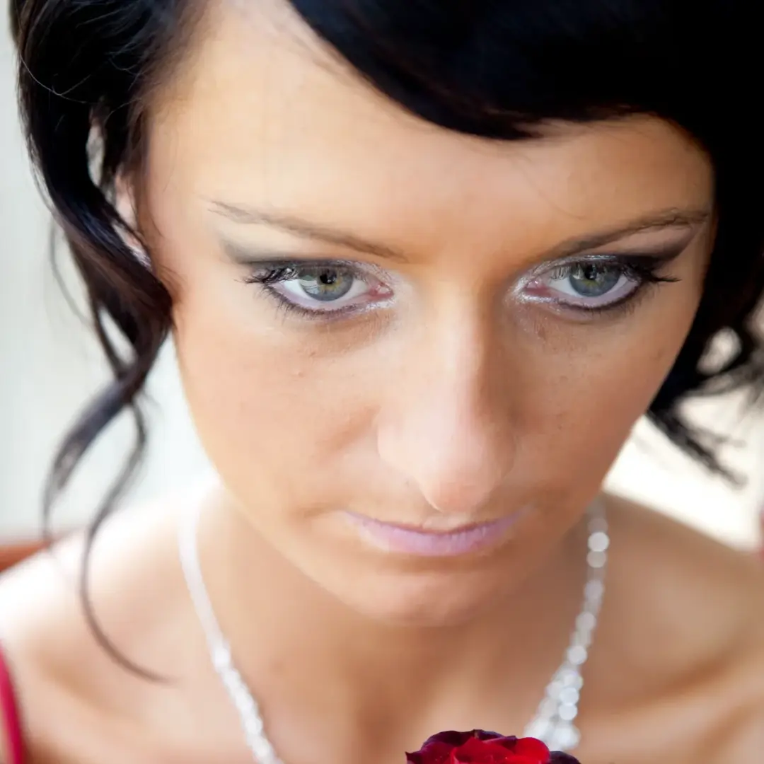 Finished bridal makeup with defined liner and a soft lip, worn with dark hair and red roses