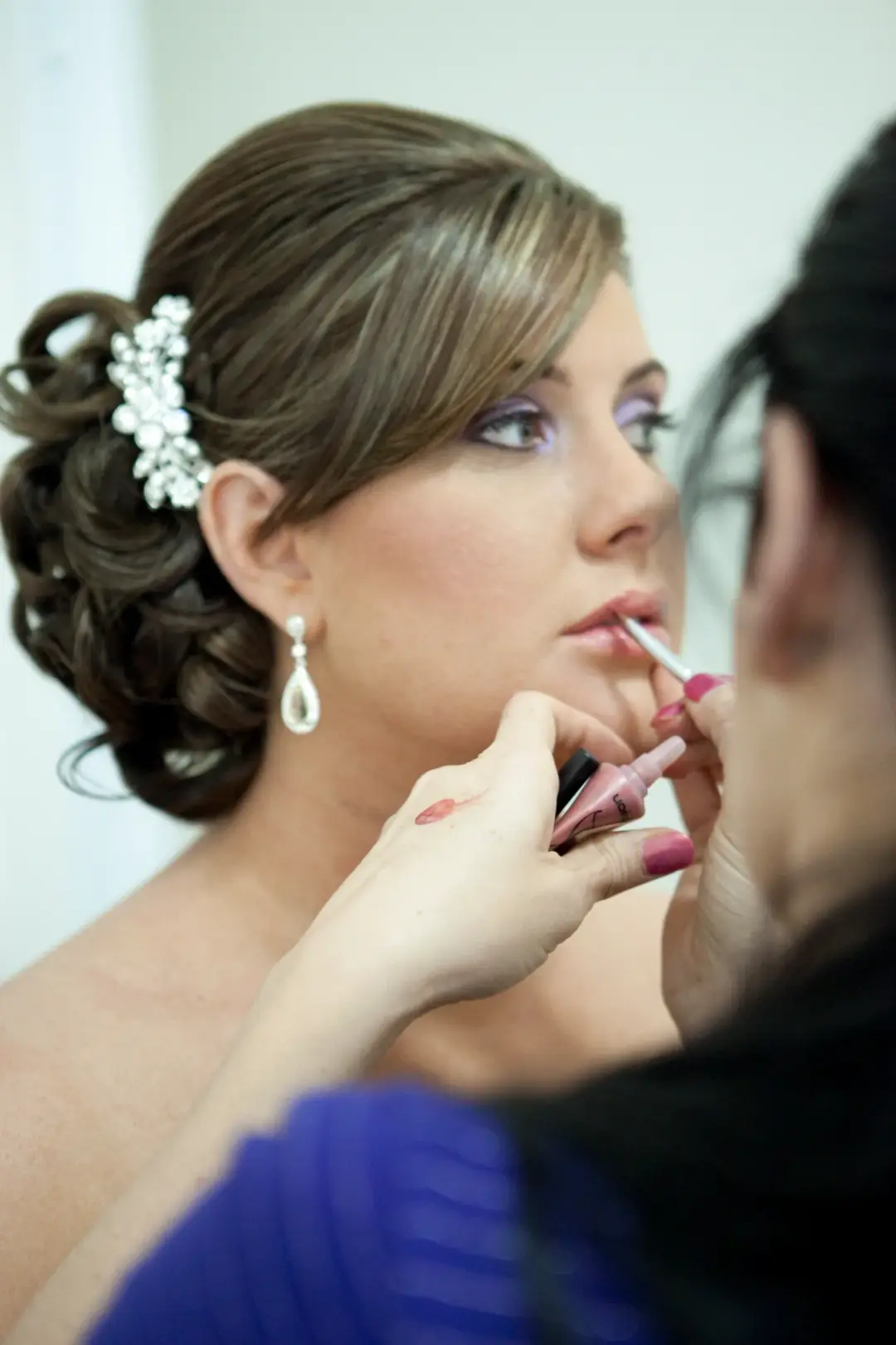 Lip colour brushed onto a bride wearing a curled updo with a crystal hairpiece and pearl drop earrings