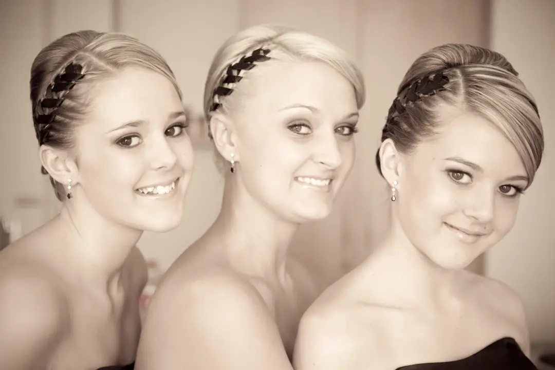 Three bridesmaids styled together, two in braided crowns and one in a smooth pinned back finish