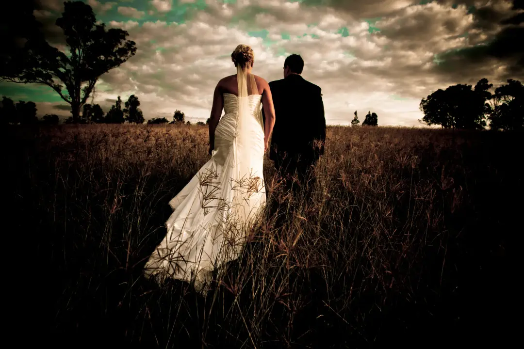 Couple walking into a paddock at dusk, the bride's hair pinned up above the back of her gown