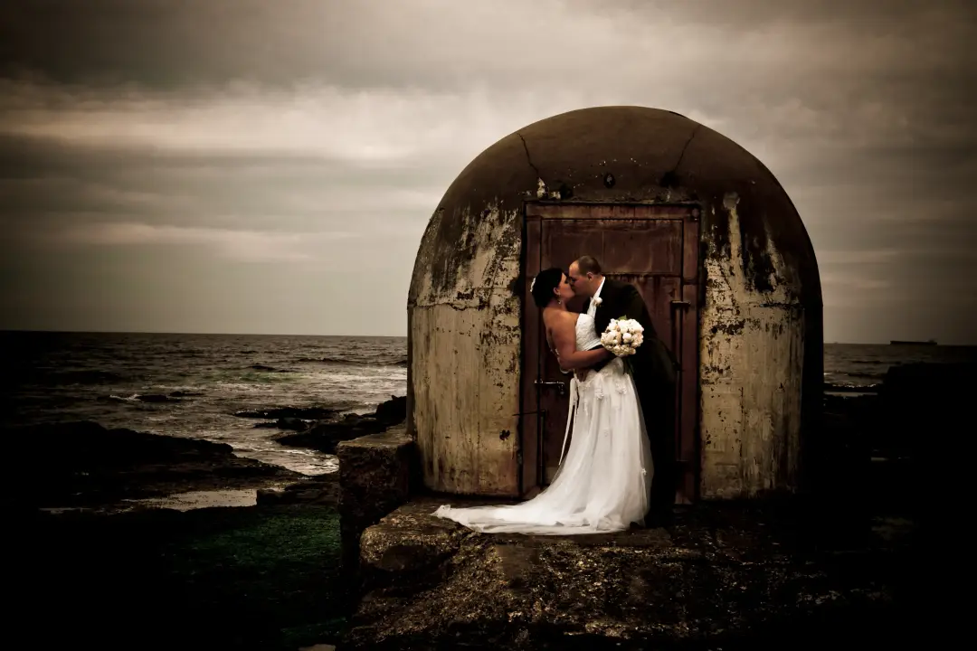 Couple eloping at a stone chapel by the ocean, the bride's hair worn long beneath a veil