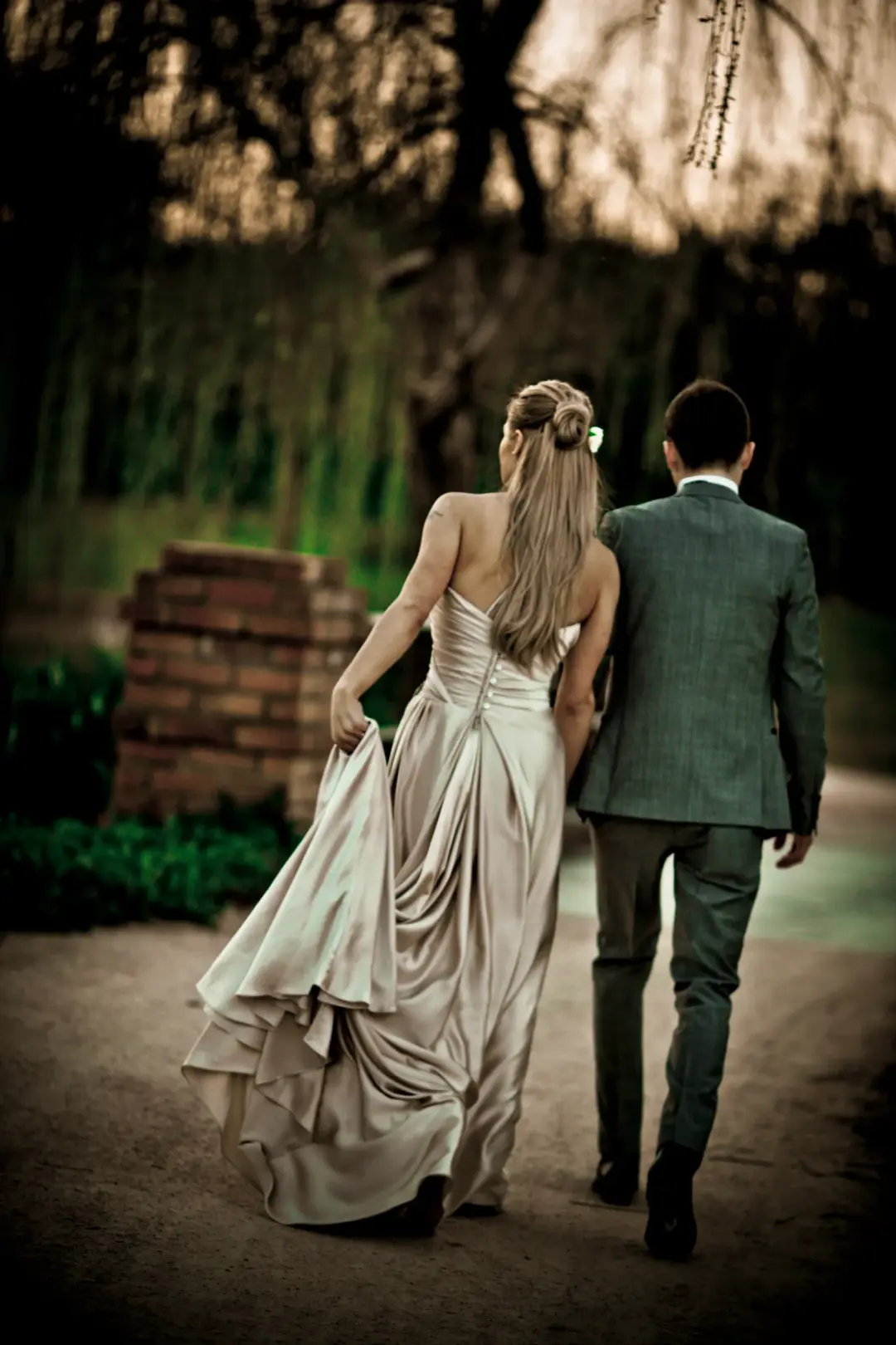 Couple walking a garden path, the bride's long hair worn down with a flower pinned at the crown