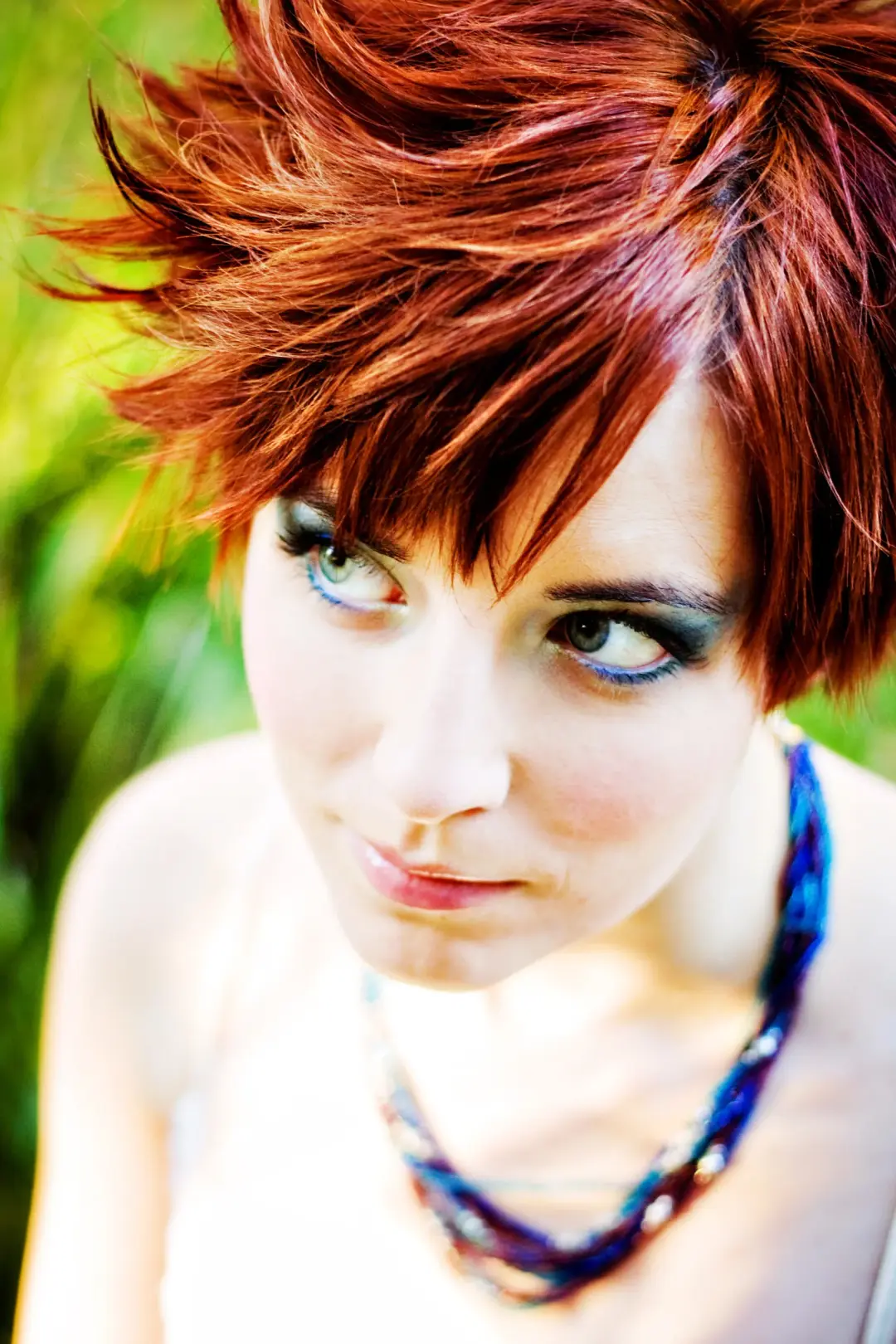 Textured short red cut styled up at the crown, worn with a bold blue and green eye
