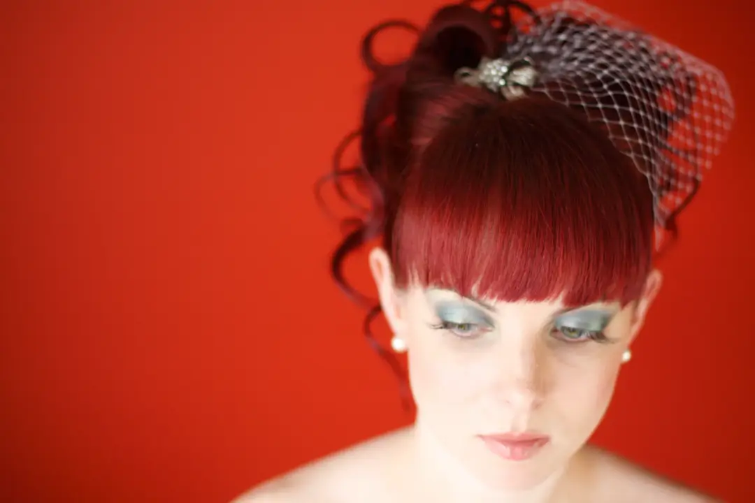 Statement eye makeup in pale aqua with a heavy lash, worn with a red updo and a birdcage veil