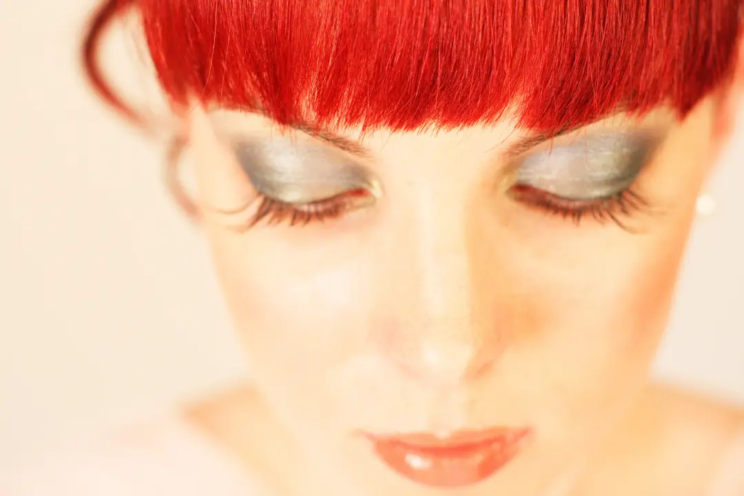Studio portrait of a silver metallic eye with heavy lashes, worn with a red fringe