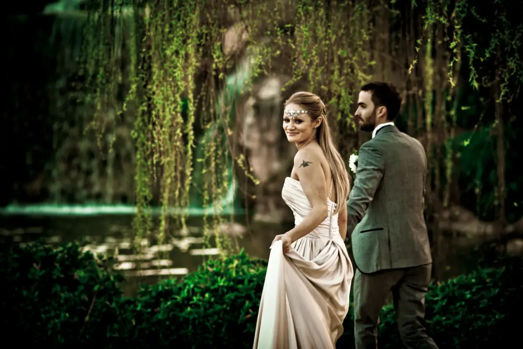 Bride glancing back over her shoulder beside her groom in a garden of hanging vines, her hair worn long and loose