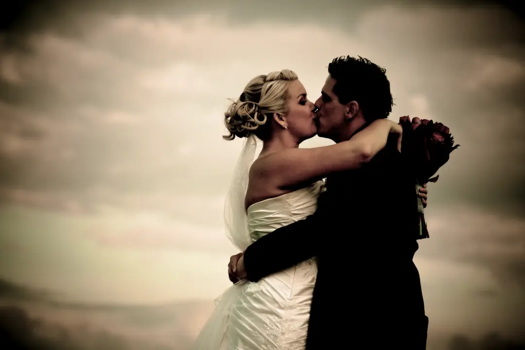 Bride and groom kissing under a wide sky, her blonde hair pinned into a low twist