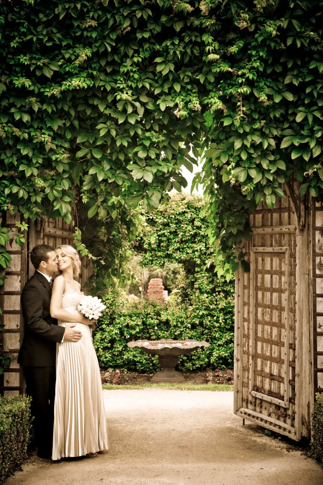 Couple under an ivy archway, the bride's blonde hair pinned into a soft updo