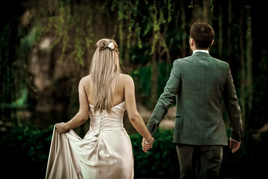Bride and groom walking away hand in hand, her long hair worn down with a hairpiece at the crown