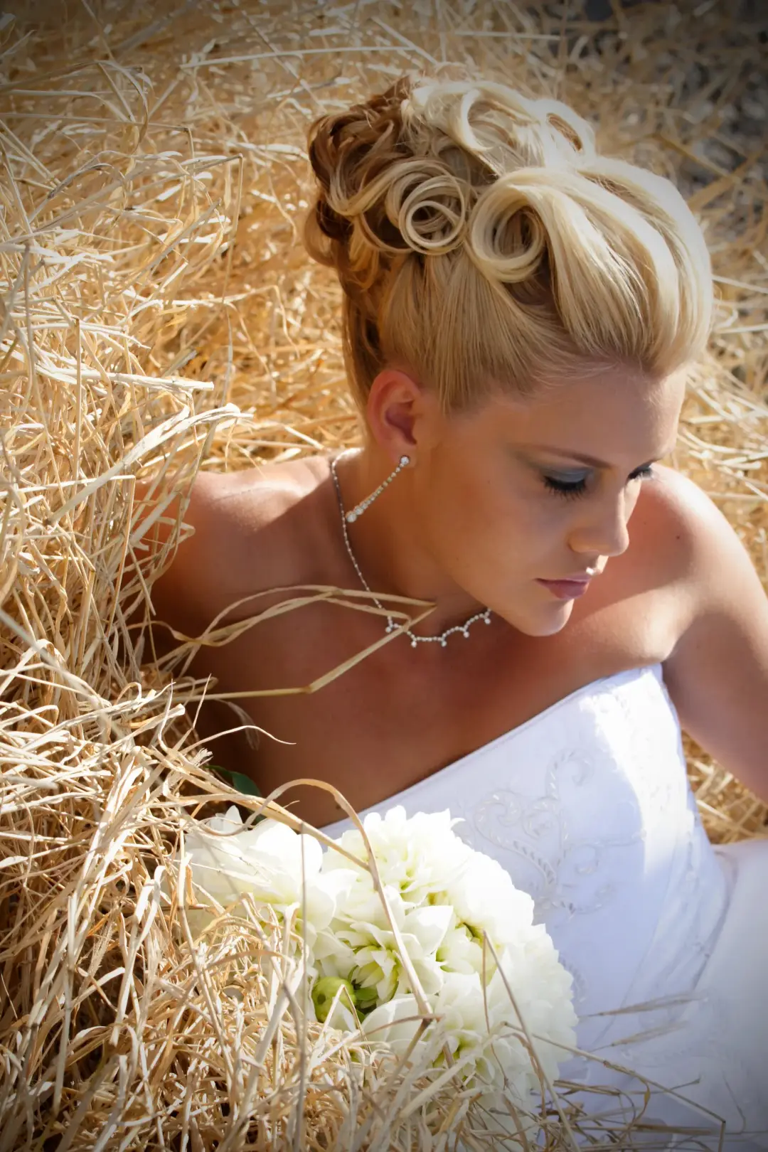 Bride in a hay field with her blonde hair rolled into a high sculpted updo