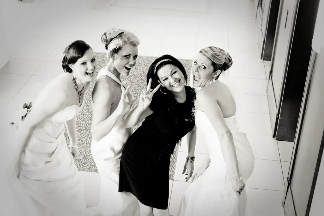 Bride, bridesmaids and their stylist laughing together, hair and makeup finished for the morning