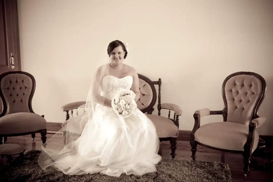 Bride seated between two armchairs with her veil spread, her dark hair pinned back neatly