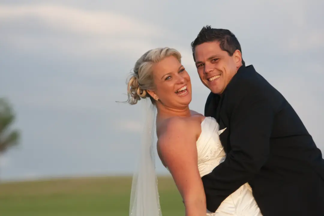 Bride and groom laughing together, her blonde hair pinned up beneath a veil