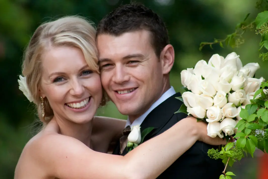 Bride and groom cheek to cheek after the ceremony, the bride wearing soft natural makeup with a white bloom pinned into her blonde hair