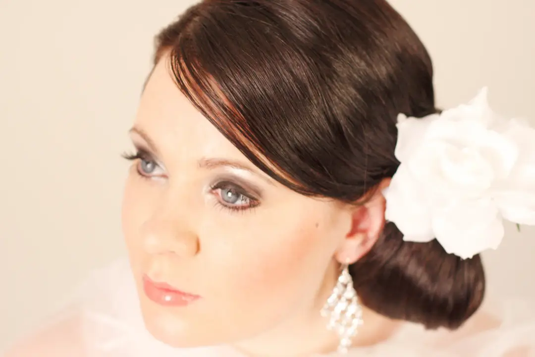 Dark hair swept into a smooth low style with a white flower, worn with a soft classic eye