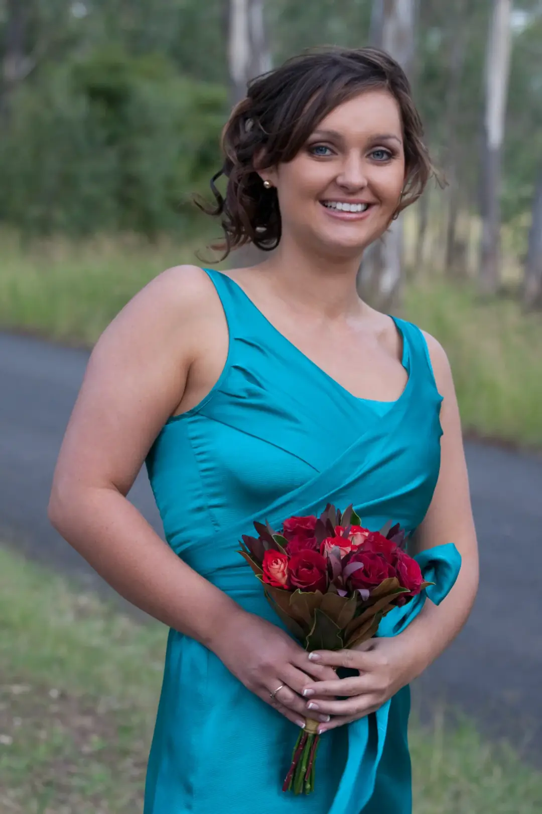 Mother of the groom in a teal dress with her hair pinned into a soft updo, holding a bouquet of native flowers