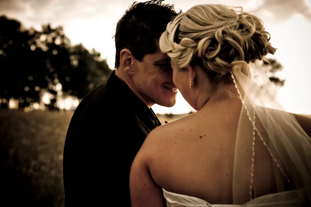 Bride and groom close together at sunset, her blonde hair pinned into a curled updo with a strand of pearls, by Amanda Frost of Bellus