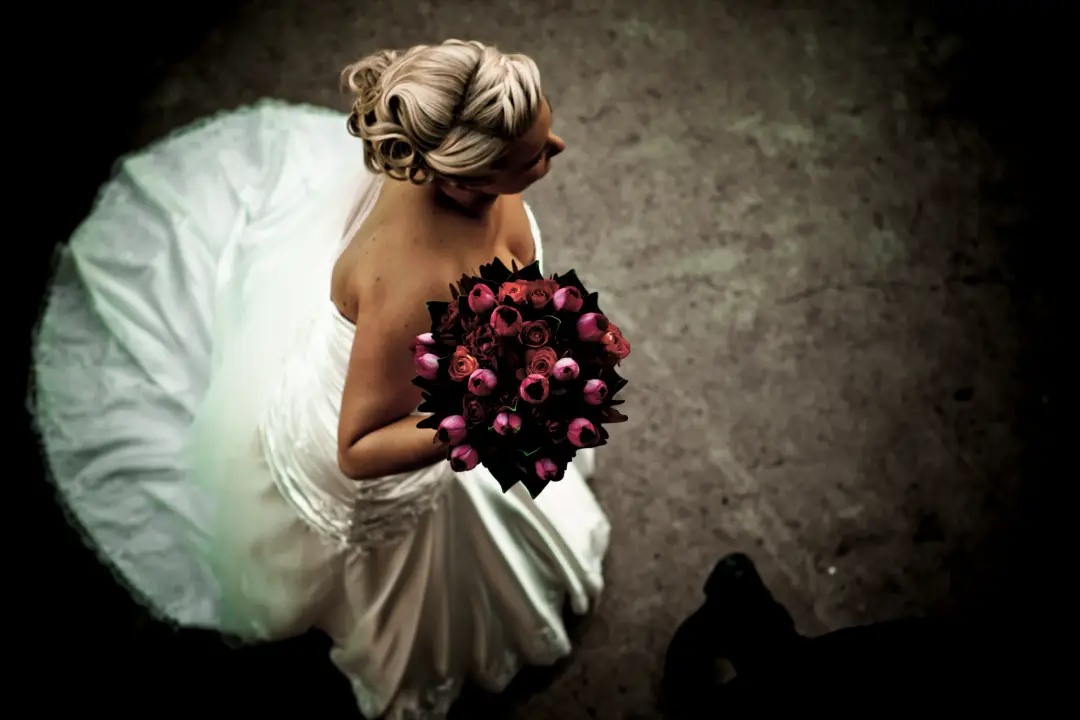 Bride from above holding a deep pink bouquet, her blonde hair pinned into a low updo, by Amanda Frost of Bellus