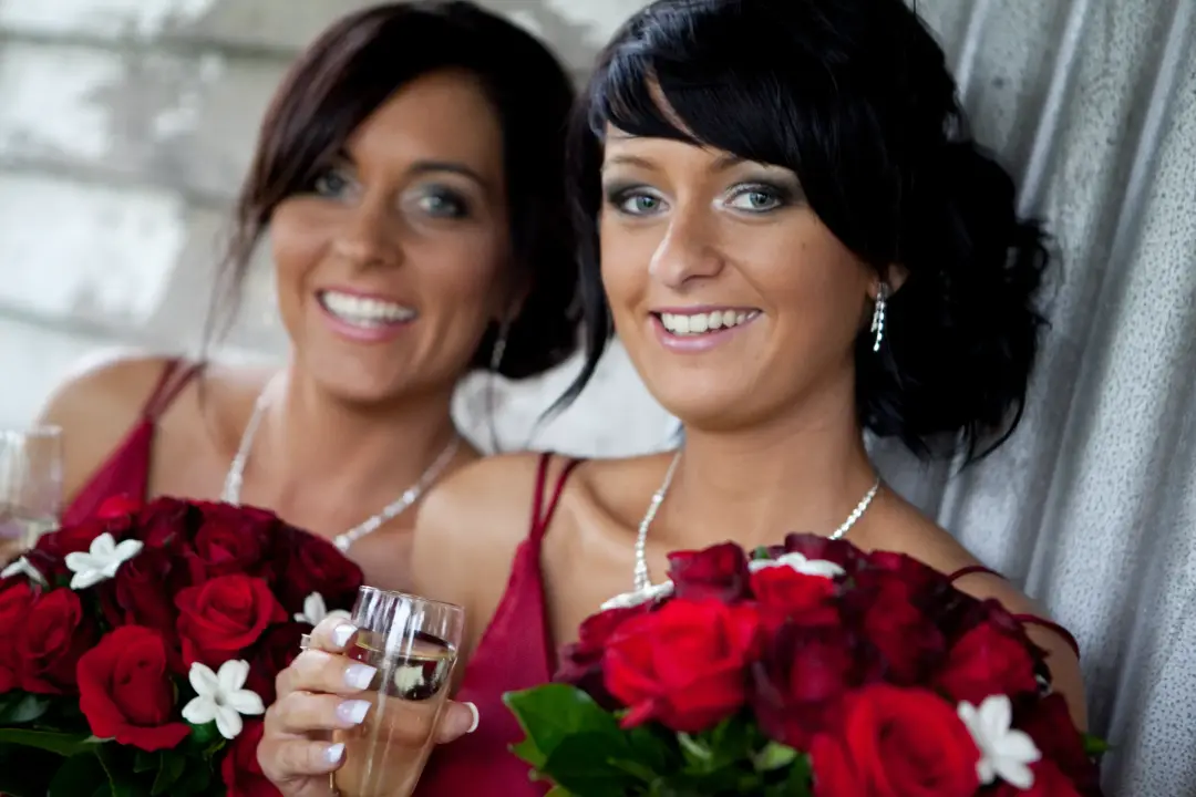 Two guests at the reception with red rose bouquets, dark hair styled long and pinned back