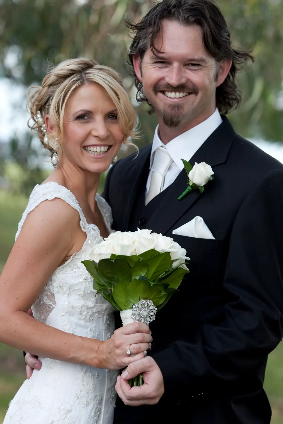 Bride and groom together outdoors, her blonde hair curled into a pinned updo with a white bouquet