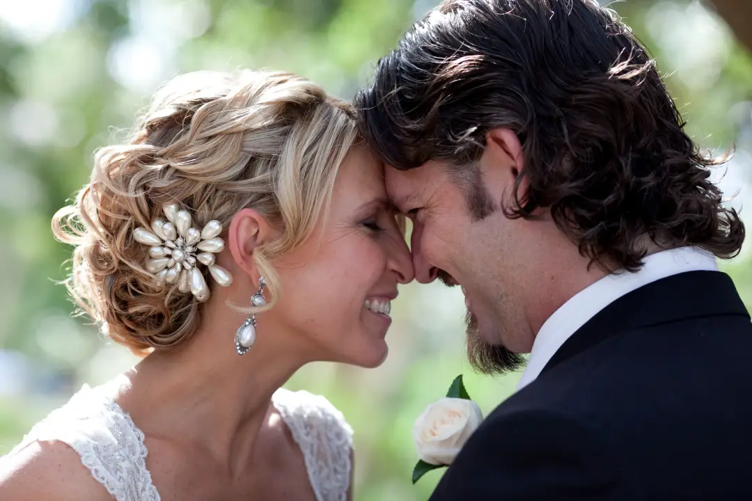 Bride and groom forehead to forehead, her blonde hair in a curled updo with a pearl hairpiece