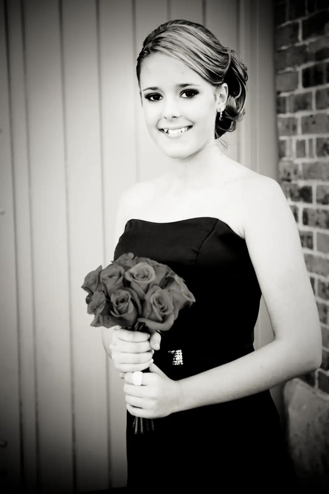 Bridesmaid in a strapless gown with her hair in a textured low updo, holding a bouquet of roses
