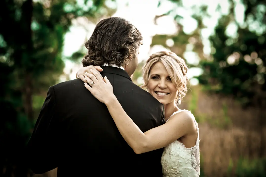 Bride looking back over her groom's shoulder, her blonde hair pinned into a soft updo
