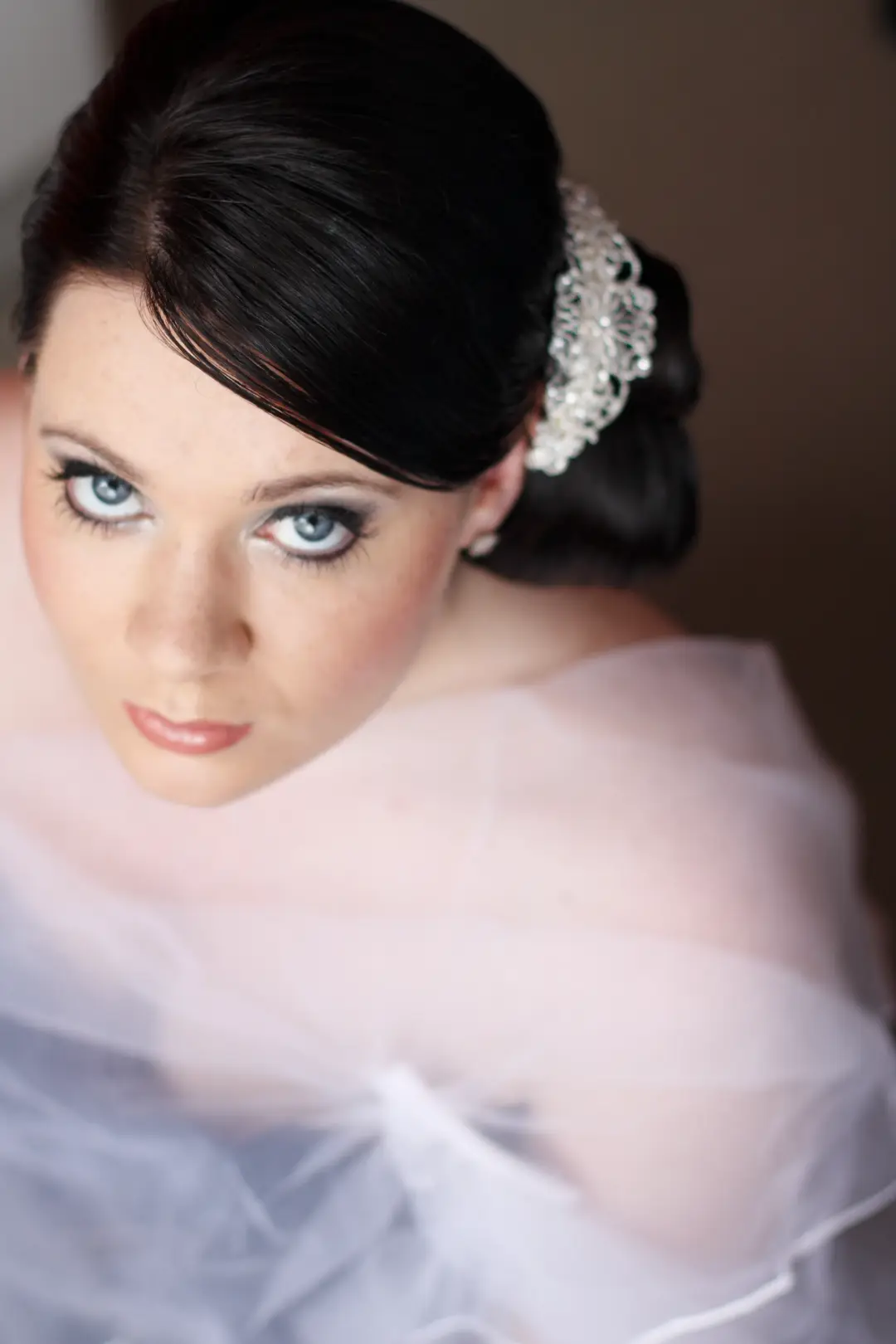 Dark haired bride in a low chignon finished with a crystal hair comb, wearing smokey eye makeup under a tulle veil