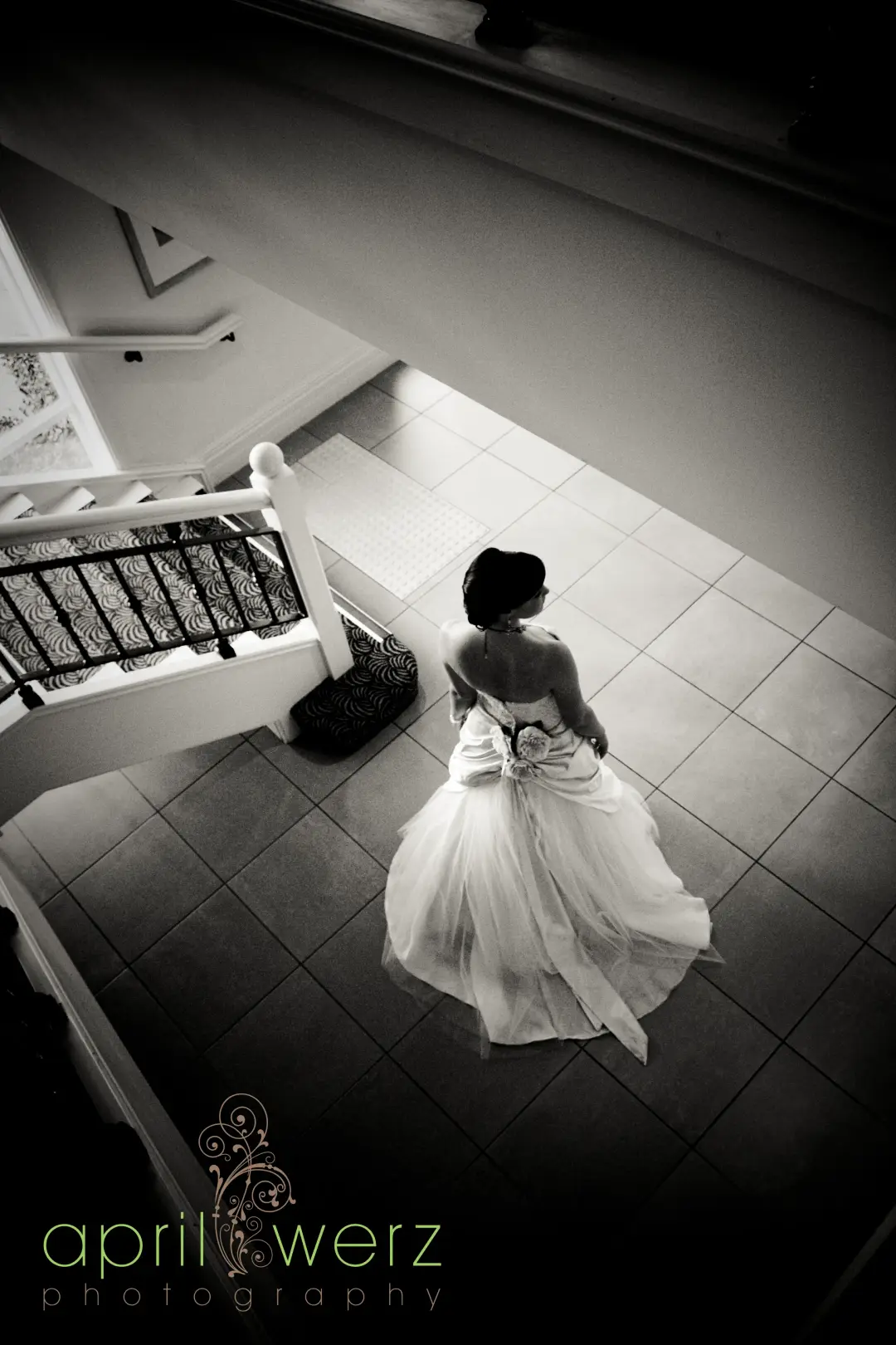 Bride photographed from the top of a staircase, her hair swept into a low updo above the open back of her gown