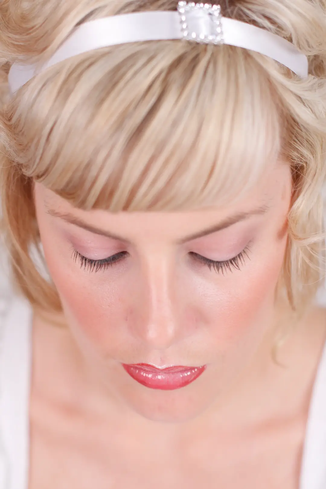 Bride with a soft blonde style and a satin headband, wearing a glossy coral lip