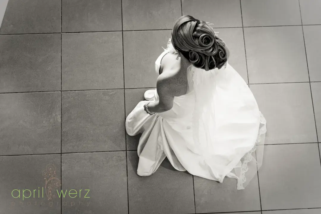 Bride seated on tiles photographed from above, her hair coiled into a sculpted dark updo