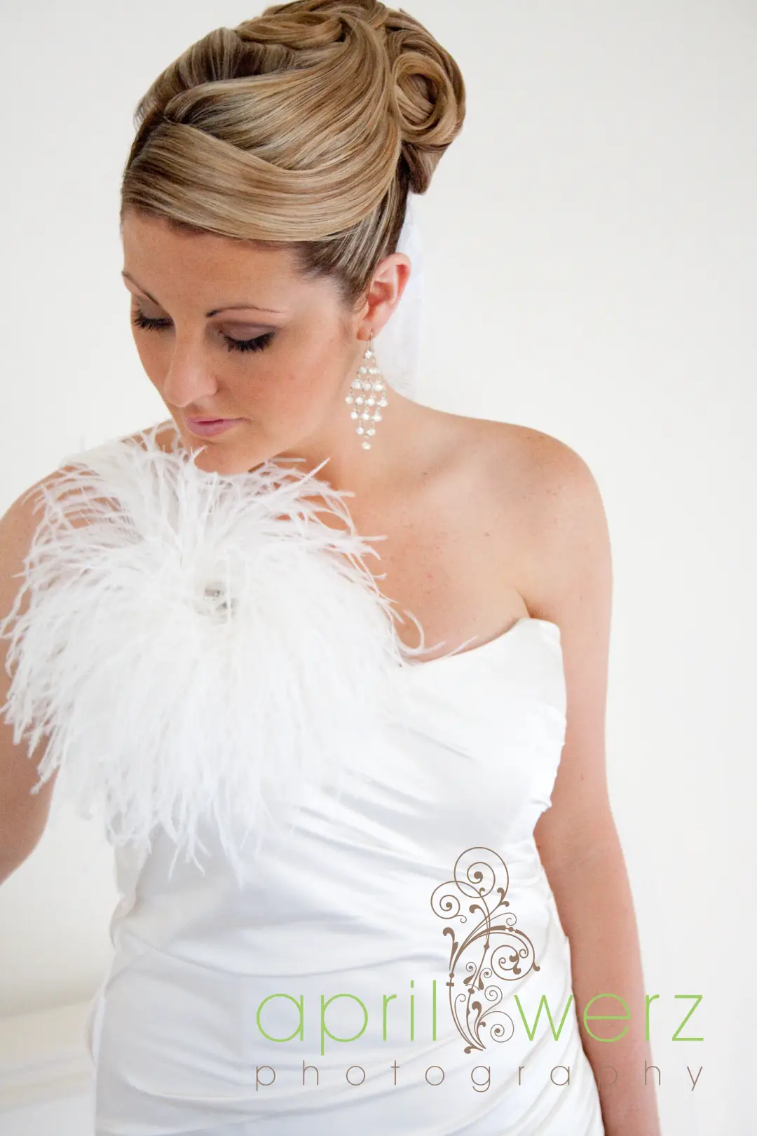 Bride in a high curled updo with a feather corsage and long diamante earrings