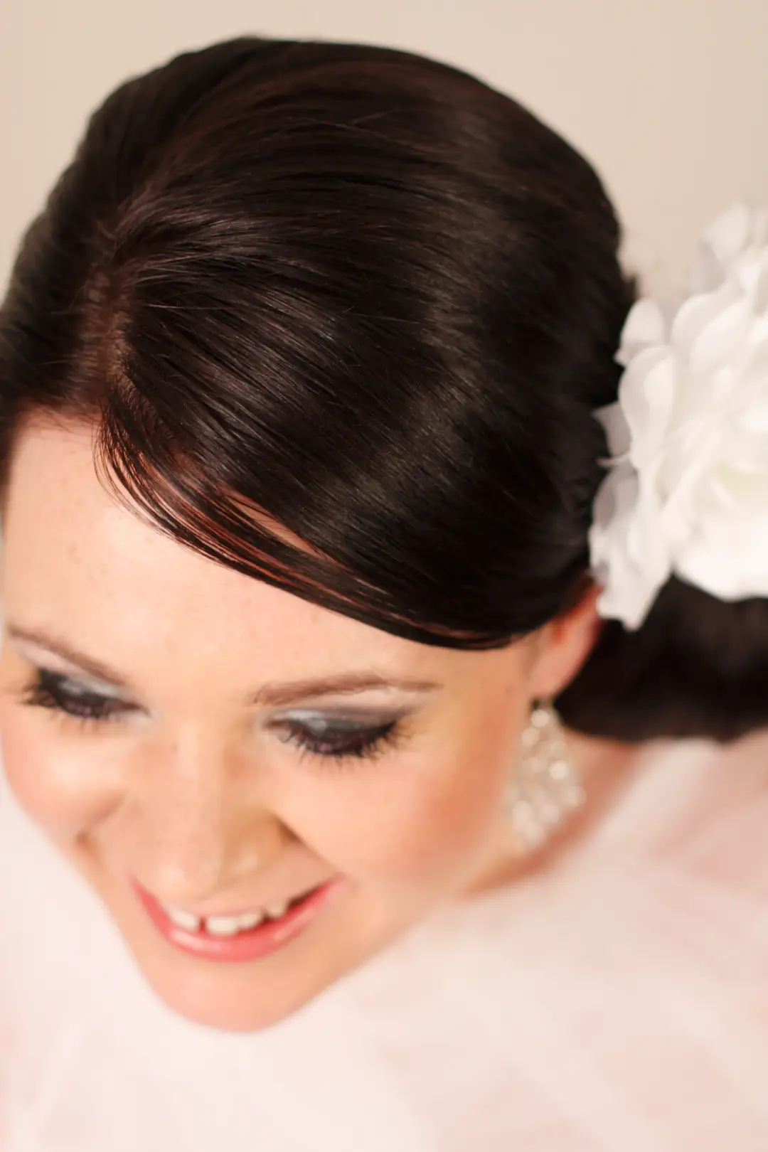 Dark hair swept into a smooth side style with a white fabric flower, worn with a silver smokey eye