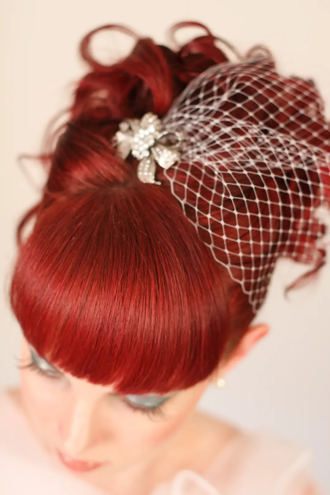 Deep red hair styled into a high curled updo with a birdcage veil and a diamante clip
