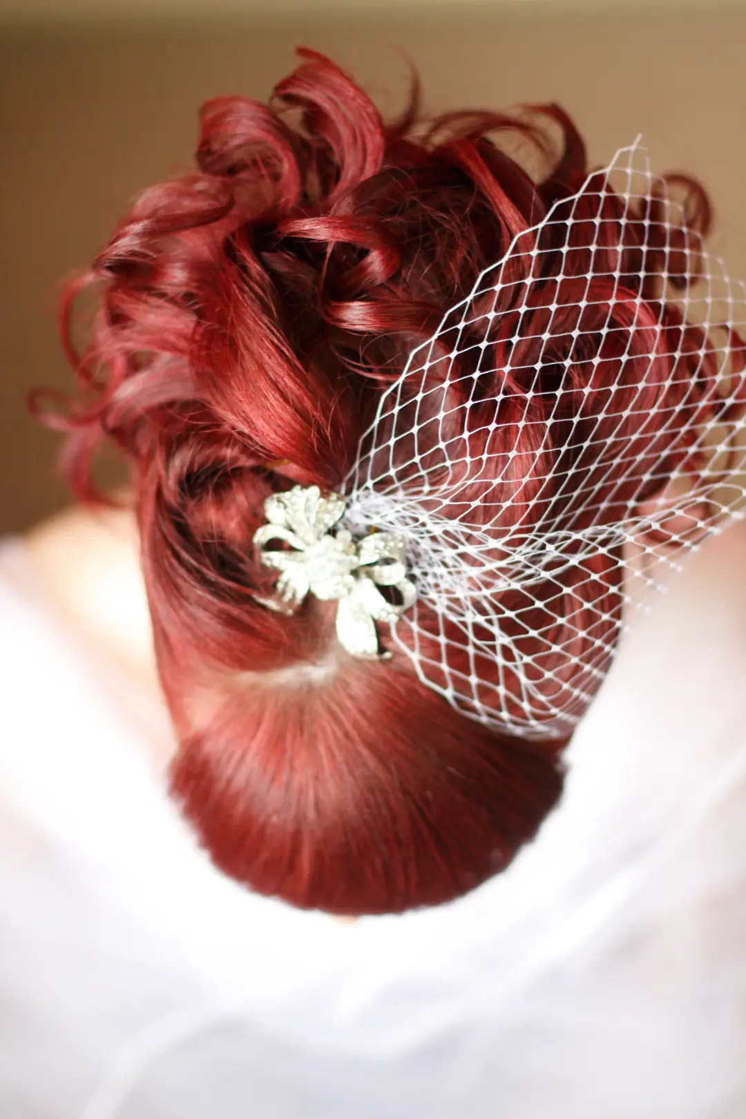 Back view of a red curled upstyle pinned with a diamante clip and a birdcage veil