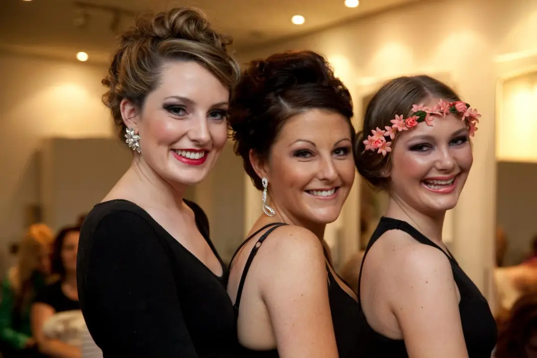 Three guests styled for an event, one in a braided updo, one pinned low and one in a flower crown