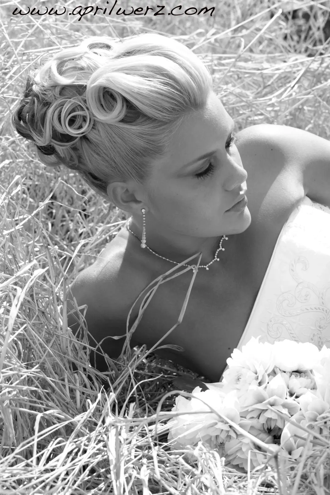 Bride lying in long grass, her blonde hair set in a curled and rolled updo