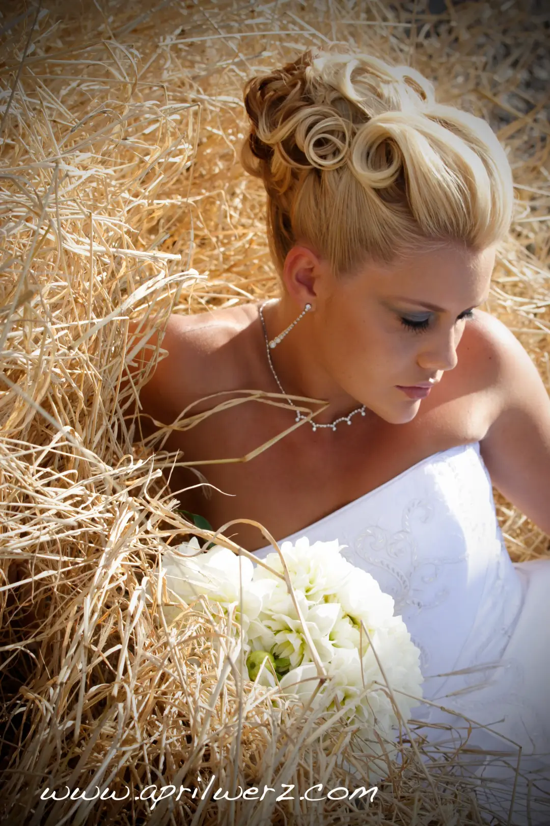 Bride resting in a hay field, her blonde hair rolled into a high curled updo