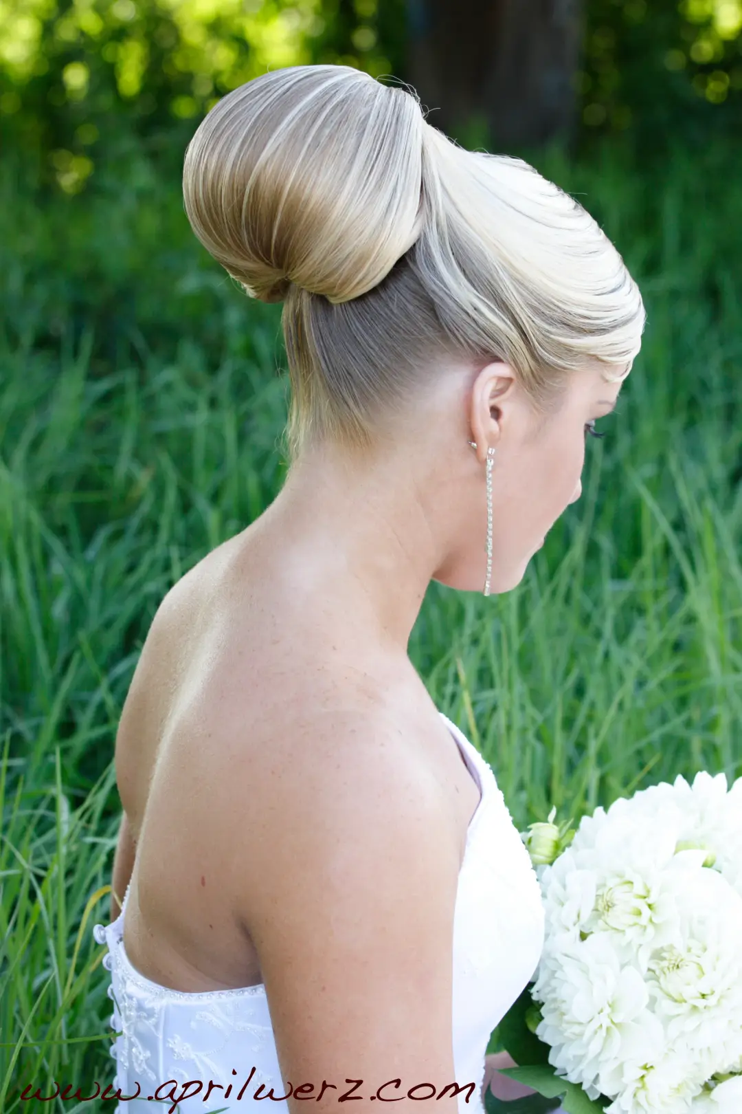 Side view of a sleek blonde high bun with a swept fringe, worn with a strapless gown