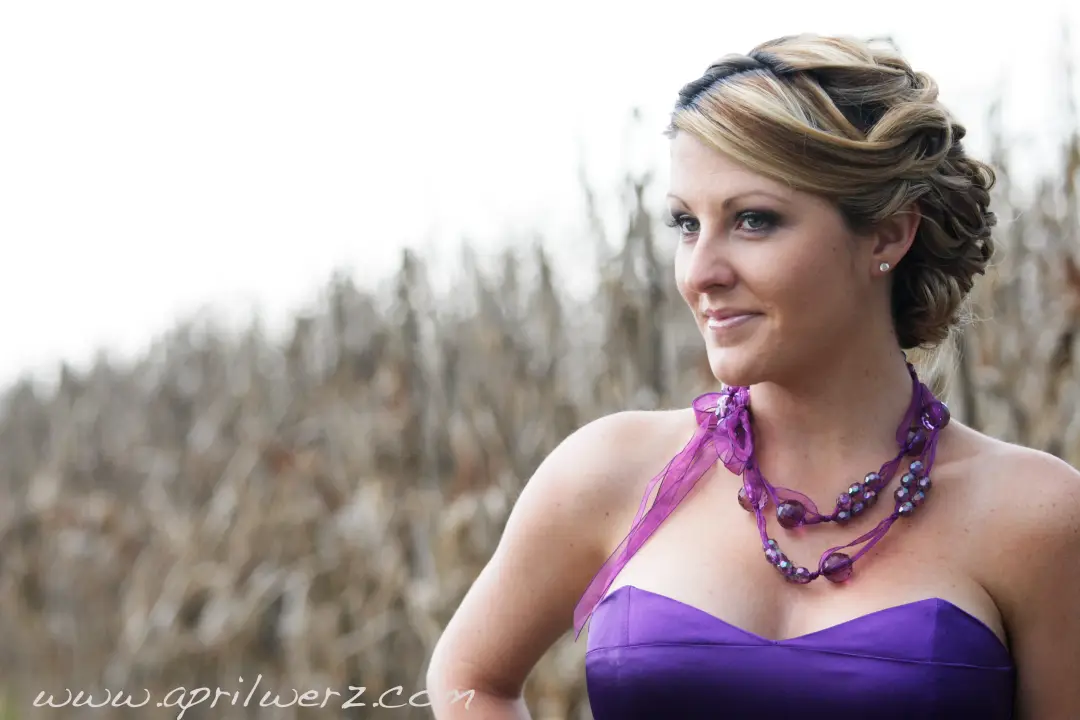 Bridesmaid in purple with her blonde hair pinned into a braided updo, wearing a bright statement necklace
