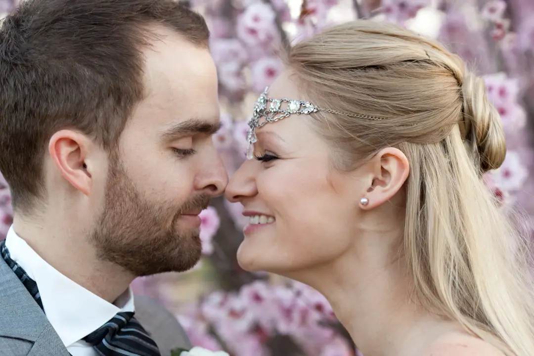 Bride and groom nose to nose under blossom, the bride wearing a crystal headpiece with her hair swept back