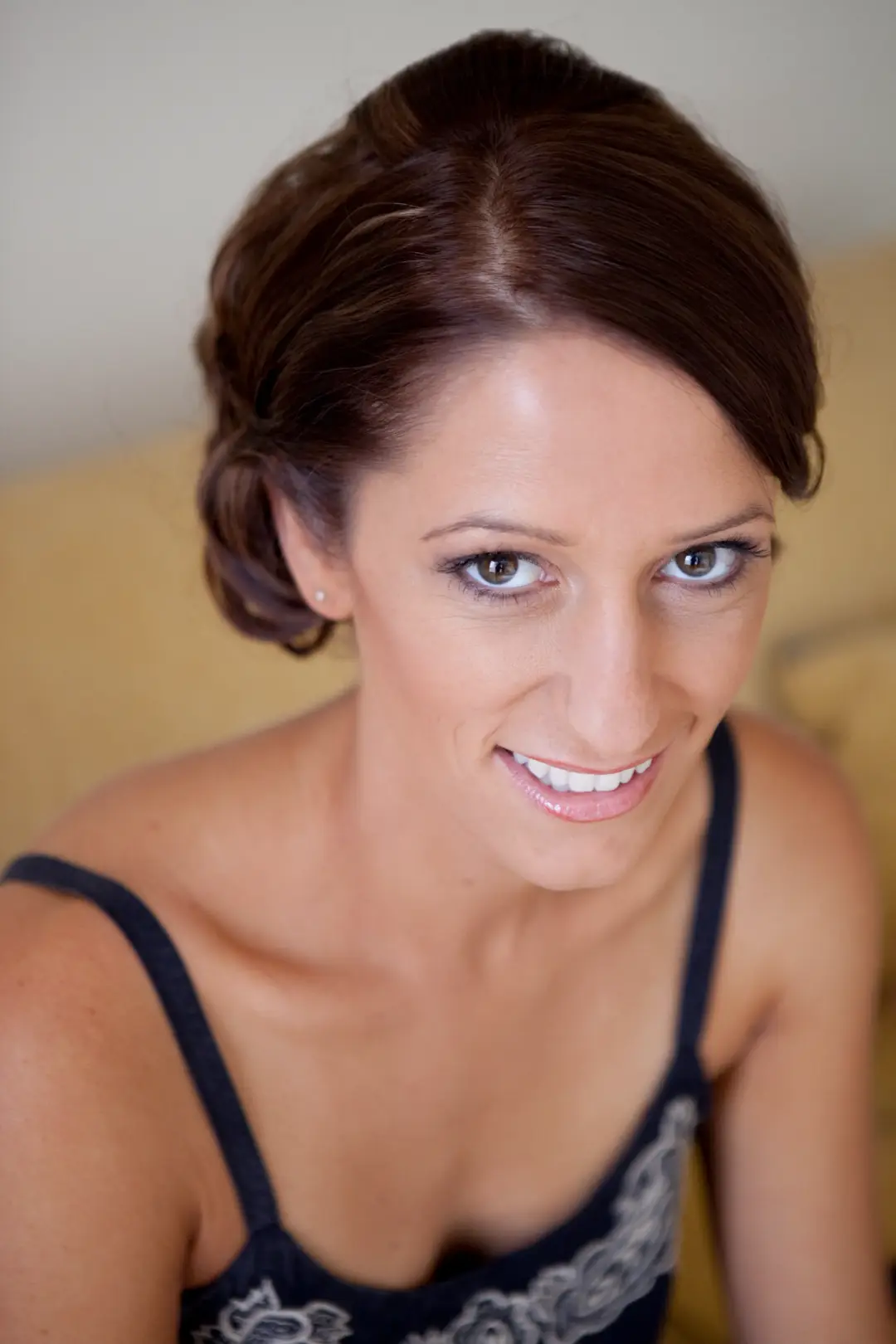 Guest with brunette hair pinned into a soft rolled updo, wearing natural glowing makeup