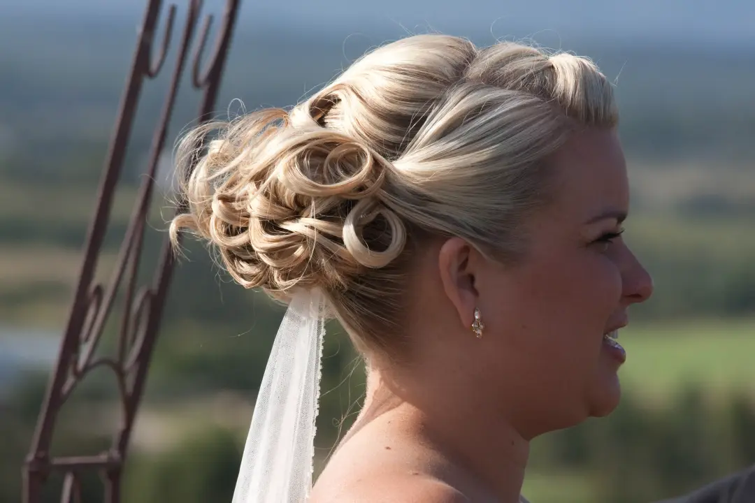 Side view of a full curled blonde upstyle with the veil pinned beneath it