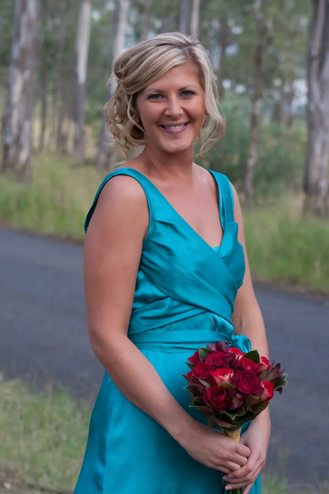 Mother of the bride in teal with a short curled style, holding a bouquet of red roses