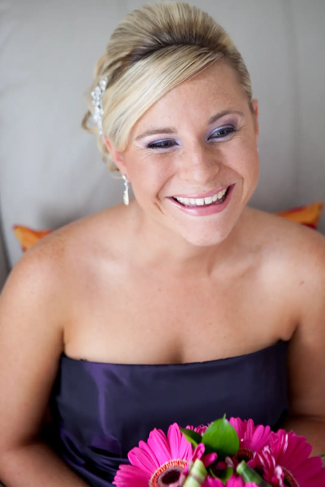 Bridesmaid in a purple gown laughing, her blonde hair pinned up with a diamante clip and a lilac eye