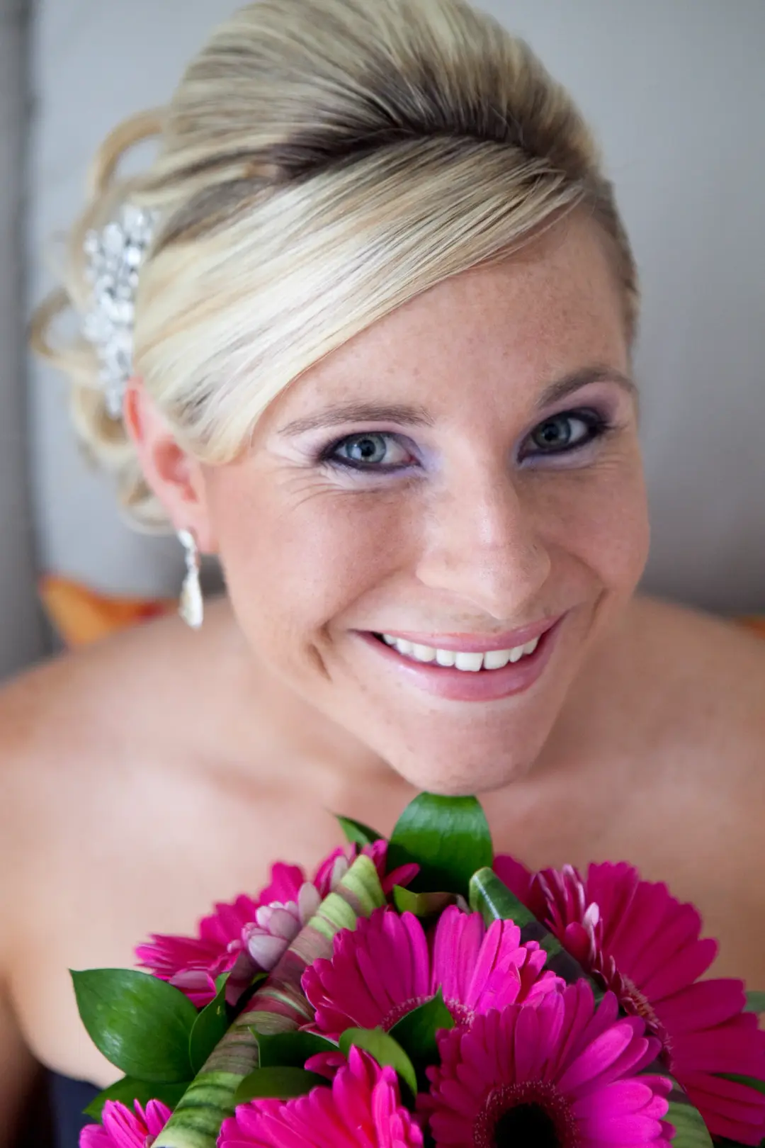 Bridesmaid in a blonde updo with a crystal hairpiece, holding pink gerberas