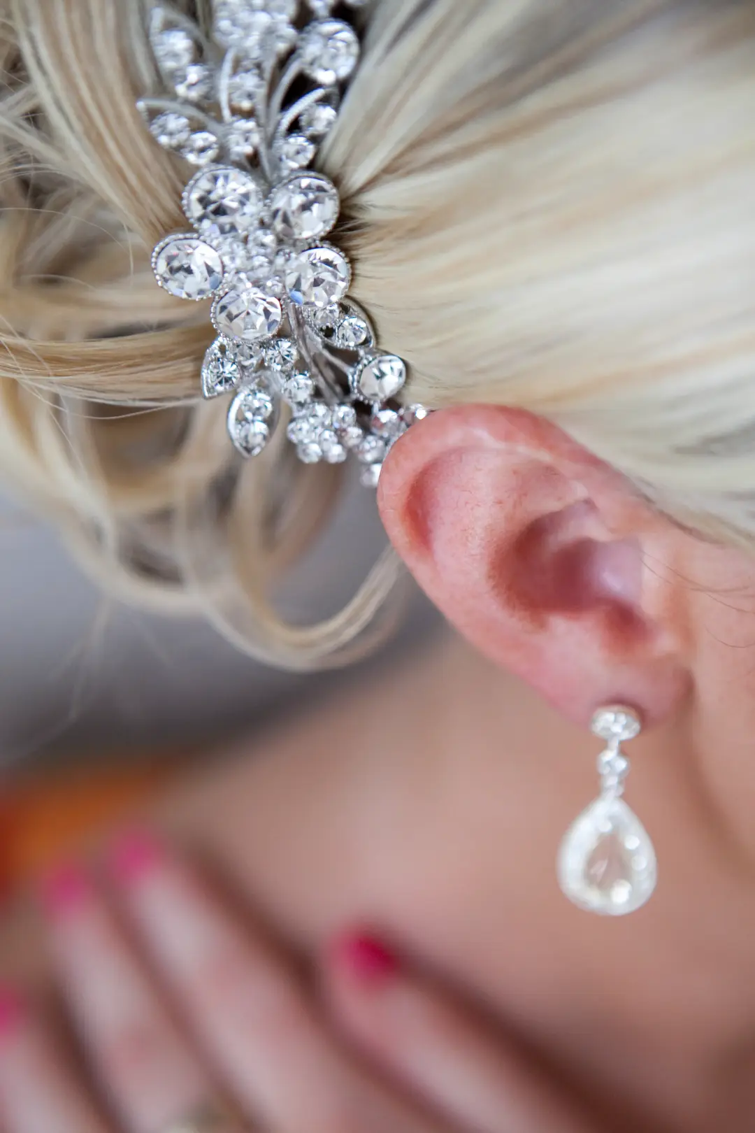 Close view of a crystal hair comb pinned into a blonde updo beside a teardrop earring